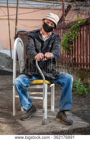 Senior Man In Protective Mask With A Cane Sitting On A Chair