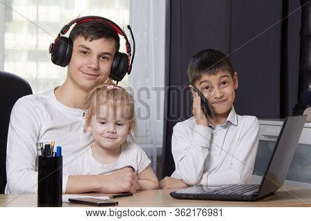 Teenager Looks At A Laptop And Writes Down A Task And Children Interfere With Learning