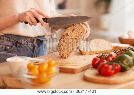Warm-toned Close Up Of Unrecognizable Woman Cutting Fresh Wholewheat Bread While Making Breakfast In