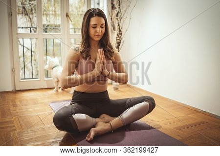 Young Woman Is Doing Yoga Meditation In The Living Room At Home. She Is Meditating On Floor Mat In M