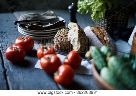 Fresh ripe tomatoes, cucumbers, assortment of homemade bread and stack of plates on blue wooden tavle served for breakfast in the morning