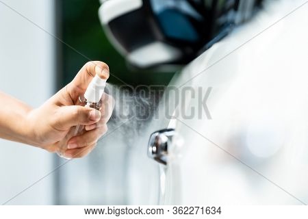 Closeup car wash clening using hand spraying alcohol, disinfectant spray on car door handle for safety prevent and protect from infection of virus and germ Covid-19 coronavirus world pandemic.