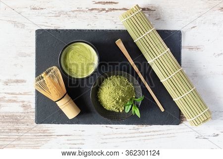 Green Matcha Tea Drink And Tea Accessories On Black Board On White Wooden Table Top View. Japanese T