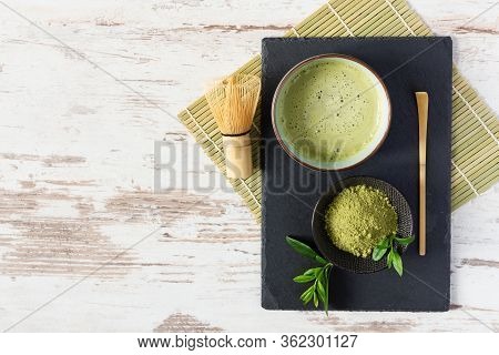 Green Matcha Tea Drink And Tea Accessories On Black Board On White Wooden Table Top View. Japanese T