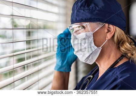 Female Doctor or Nurse On Break At Window Wearing Medical Face Mask and Goggles.
