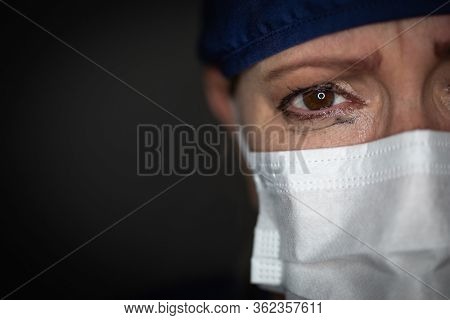 Tearful Stressed Female Doctor or Nurse Wearing Medical Face Mask on Dark Background.