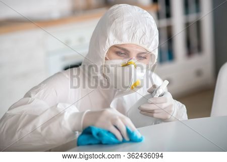 Woman In White Workwear And Protective Gloves Disinfecting The Surface