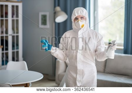 Woman In White Workwear And Protective Gloves Holding Antiseptic Liquid And A Duster
