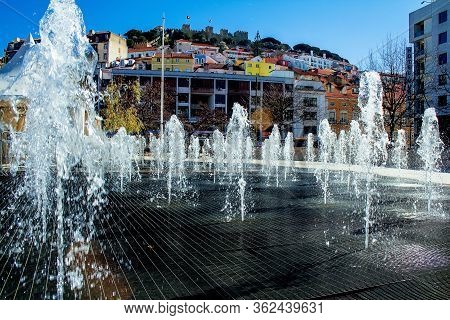 Fantan. Jets Of Water Beat From The Ground. In The Background On The Hilly Terrain Of The House. Lis