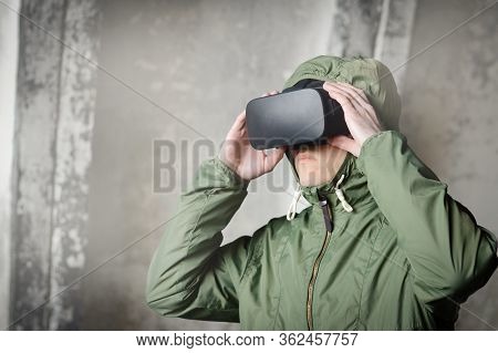 Young Gamer With Virtual Reality Headset In A Green Protective Jacket With A Hood, A Serious Teenage