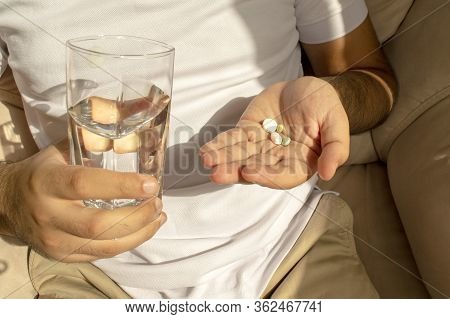 Man In White T-shirt Holds Many Pills And Glass Of Water In Hands. Young Man Holds Medicines, Oral M