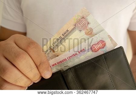 Uae National Currency. Money Banknotes. Man In White T Shirt Put Dirham Banknotes Into Black Wallet.