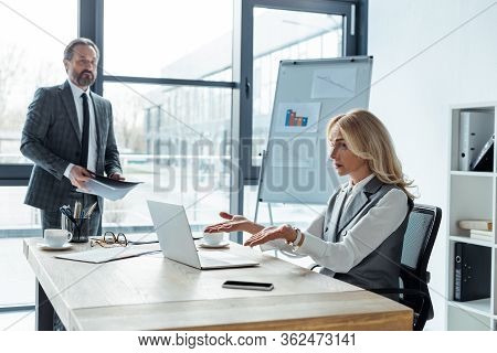Selective Focus Of Confused Businesswoman Looking At Laptop Near Businessman Holding Paper Folder In