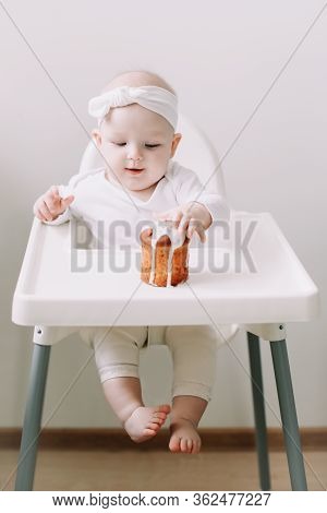 Cute Baby In A Baby Chair Enjoys Eating The Cake With His Hands. Baby With A Birthday Cake On White 
