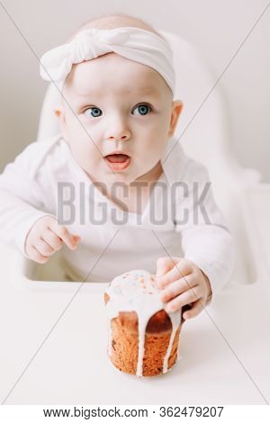 Cute Baby In A Baby Chair Enjoys Eating The Cake With His Hands. Baby With A Birthday Cake On White 