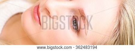 Close-up Of Young Charming Woman Laying With Painted Shape For Eyebrows. Blonde Lady At Cosmetologis