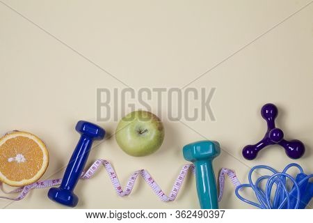 Healthy Lifestyle Concept. Blue And Green Dumbbells, Measurement, Orange, Apple And Jump Rope On Yel