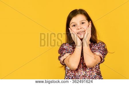 Precious Face. Child Pulls Her Cheeks Up In Affection. Girl Cute Smile On Yellow Background. Childho