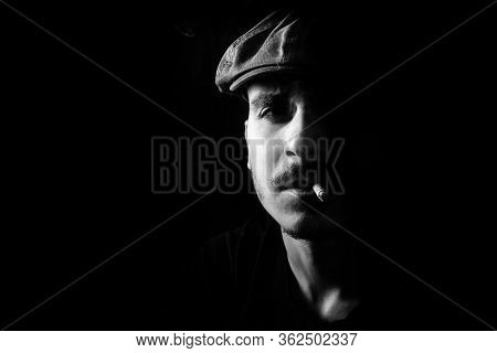 Black And White Portrait Of Cute Young Guy With Moustache And A Hat On Black, Dark Background Smokin