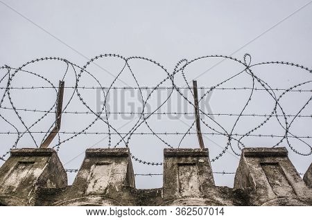 Concertina Wire Placed On The Top Of A Wall. Grey Cloudy Sky