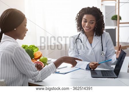 Personal Nutrition Plan. African American Woman Dietologist Consulting Patient, Using Laptop, Clinic