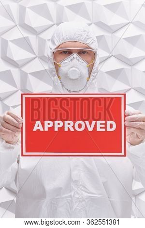 COVID-19 concept. A doctor in a protective suit holds a sign approved on a white background. Copy space.
