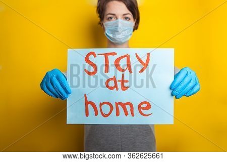 Stay At Home. A Woman In A Medical Mask And Rubber Gloves Holds A Sign Reminding You To Stay Home An