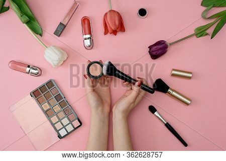 Girl Holds Makeup Brush Set Of Cosmetics And Flowers On Pink Background