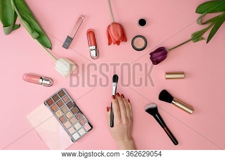 Girl Holds Makeup Brush Set Of Cosmetics And Flowers On Pink Background
