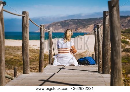 Adult Female Tourist Sitting On Path Leading To Praia Do Guincho Beach. Cascais, Portugal. This Is P