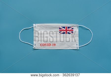 Medical Mask With The Flag Of Great Britain And The Inscription Covid-19 On A Blue Background