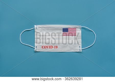 Medical Mask With The Flag Of Usa And The Inscription Covid-19 On A Blue Background