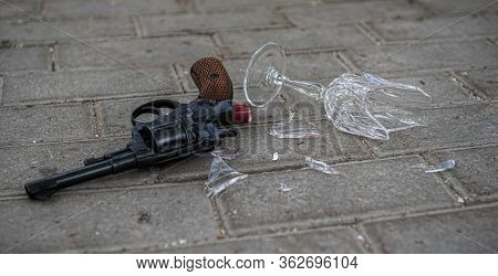 On The Tile On The Ground Lies A Revolver And A Broken Glass Of Wine. Shards Fray Nearby