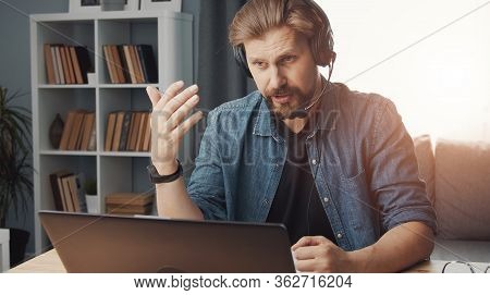 Casual-dressed Man Teleworking Sitting In Front Of Computer With Headset On, Selfisolation, Epidemic