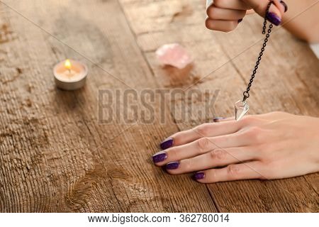 The Pendulum On A Chain With A Natural Crystal In Hands On A Background Of Wood Texture With Burning