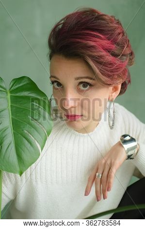 Beautiful Lady In White Sweater, Silver Earrings, And Braclet Sitting Near Green Palm Tree And Looki