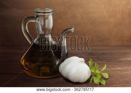 Horizontal View Of An Oil Pourer With Olive Oil, Garlic Head And Parsley On A Table And Wooden Backg