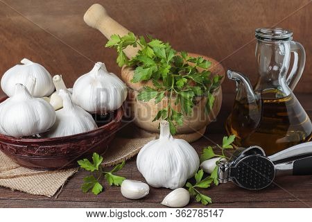 Still Life In Horizontal View With Mortar With Parsley, Bowl With Garlic Heads, Oil Pourer And Garli