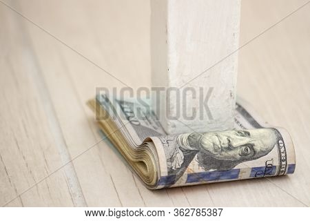 A Pack Of American Dollars Under A Table Leg On A Gray Floor Background. Depreciation Of Money, Econ