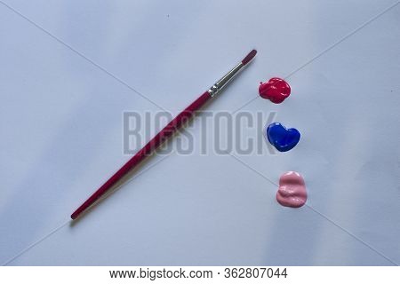 A Paint Brush With Red, Blue And Pink Paint On A Table