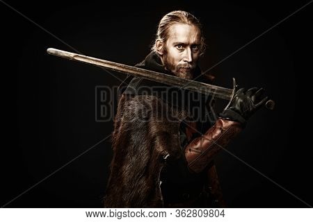 Portrait of a medieval knight in armour and with a sword over black background. Knight Templar. Historical reenactment.