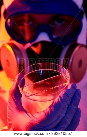 COVID-19 or 2019-nCoV. Close-up portrait of a scientist microbiologist in a protective PPE suit showing the blood test in a Petri dish.