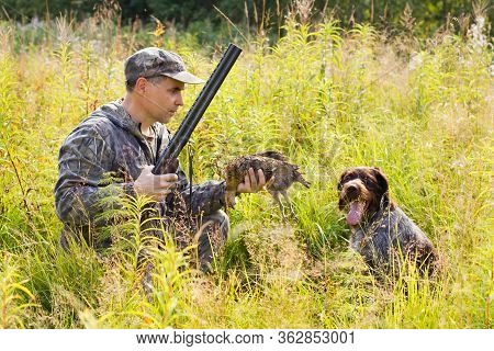 The Hunter Holds In His Hand A Downed Grouse Which Was Brought By His Dog (german Wirehaired Pointer
