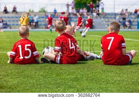 Junior Level Kids Sports Team Sitting On Grass Field. Football Soccer Children Players Standing Toge