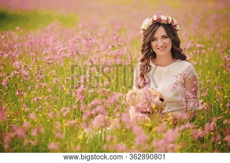Portrait Of A Pregnant Woman With Teddy Bear In Fieid Of Pink Flowers. Young Beautiful Pregnant Girl
