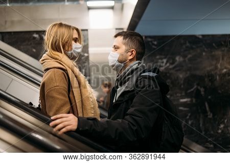 Side View Of Hugging Man And Woman In Medical Masks On Escalator In Subway. Coronavirus Pandemic.