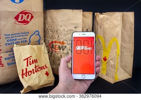 Calgary, Alberta. Canada. April 24, 2020: A Person Holding An Iphone Plus With The Skip The Dishes A