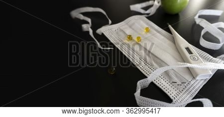 With White Medical Objects Located In A Corner On A Dark Background, A Protective Medical Mask With 