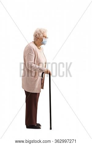 Full length profile shot of an elderly woman with a cane wearing a protective face mask isolated on white background