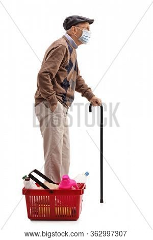 Full length profile shot of an elderly man with a protective face mask and a shopping basket full of groceries isolated on white background